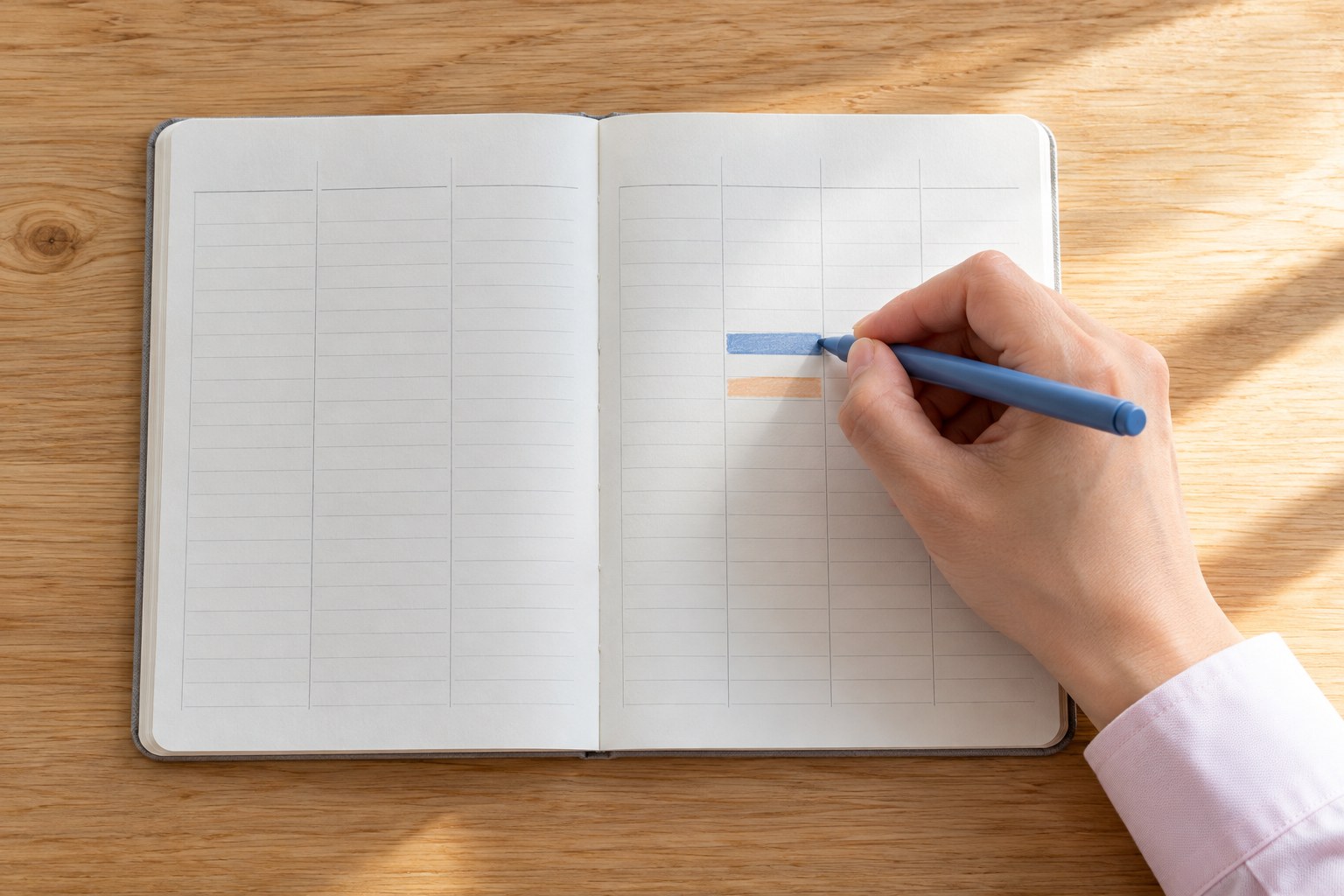 朝のテーブルで、罫線の手帳に短い帯を引いて勤務時間を書き込む手